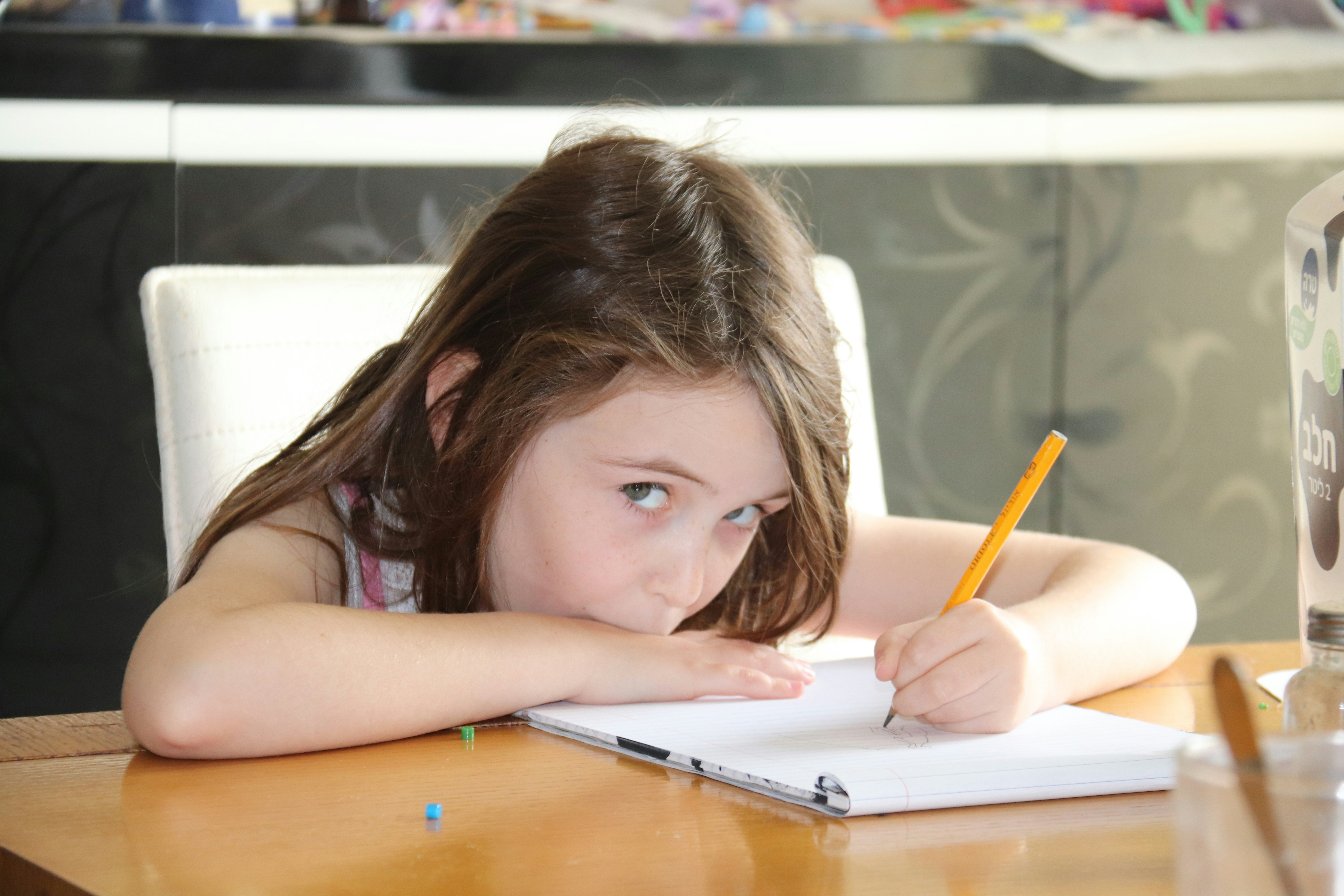 A young student writing at a table with a pencil