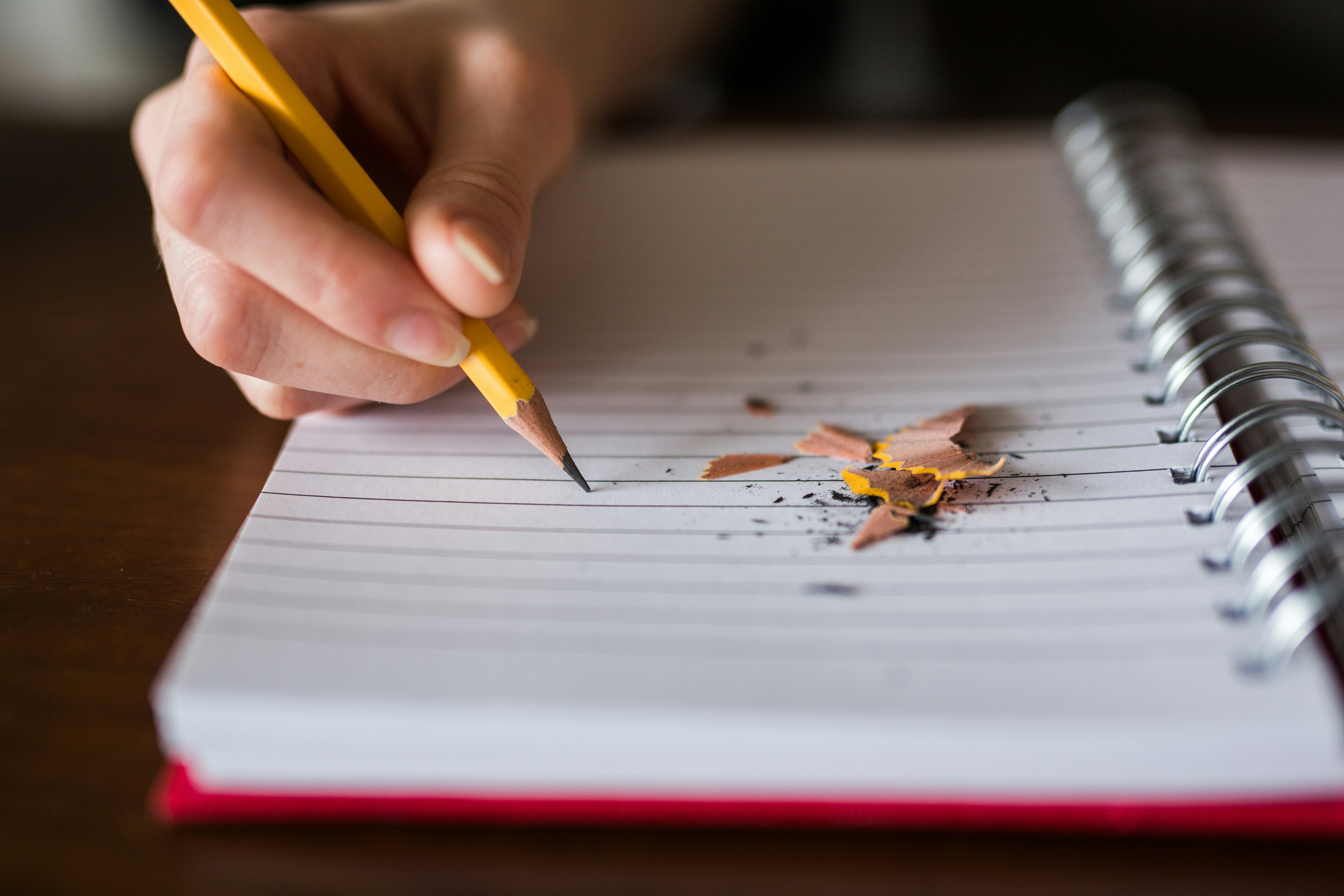 A hand writing in a lined notebook with a freshly sharpened pencil